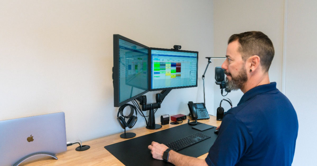 Owner standing at 2 monitor screens looking at reports and schedules for his exterior cleaning business