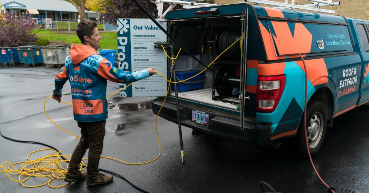 Technician employee running a hose from work truck while doing an exterior cleaning job