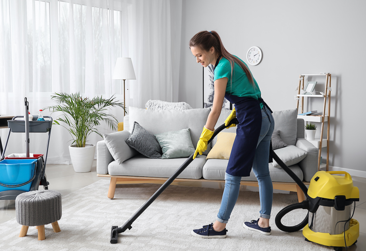 Female carpet cleaner with commercial vacuum cleaner in room