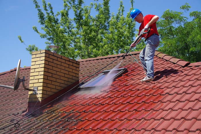 Pressure washing a red tile roof.
